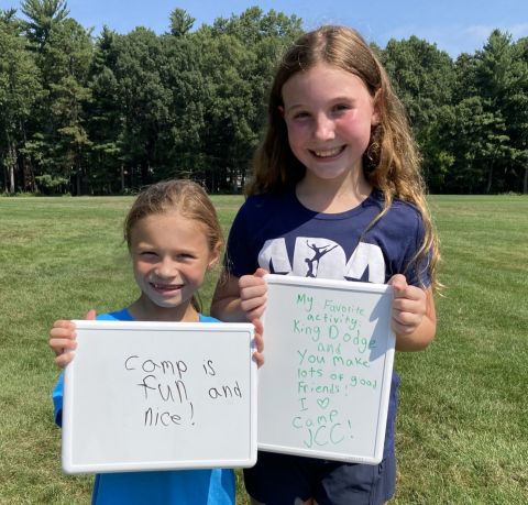 Two campers holding white boards with writing about what they love to do at camp