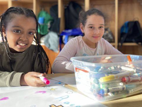 Two young girls smiling at the camera while coloring