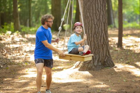 A camp counselor guides a camper on the low ropes course